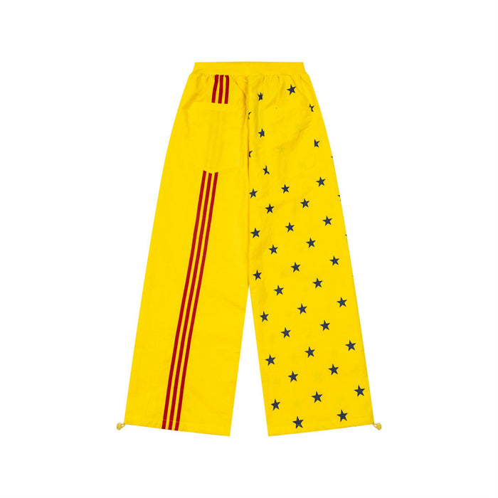 Yellow wide-leg track pants with navy star print on one leg and three red side stripes on the other