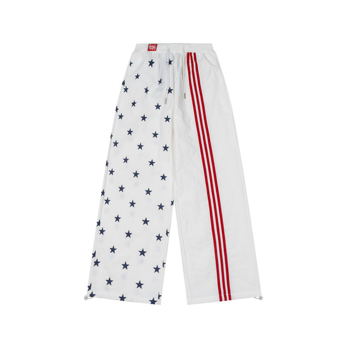 White wide-leg track pants with navy star print on one leg and three red side stripes on the other