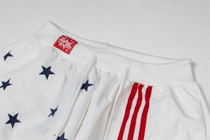 Close-up of white track pants showing ribbed waistband, navy stars, red triple stripes, and drawstring