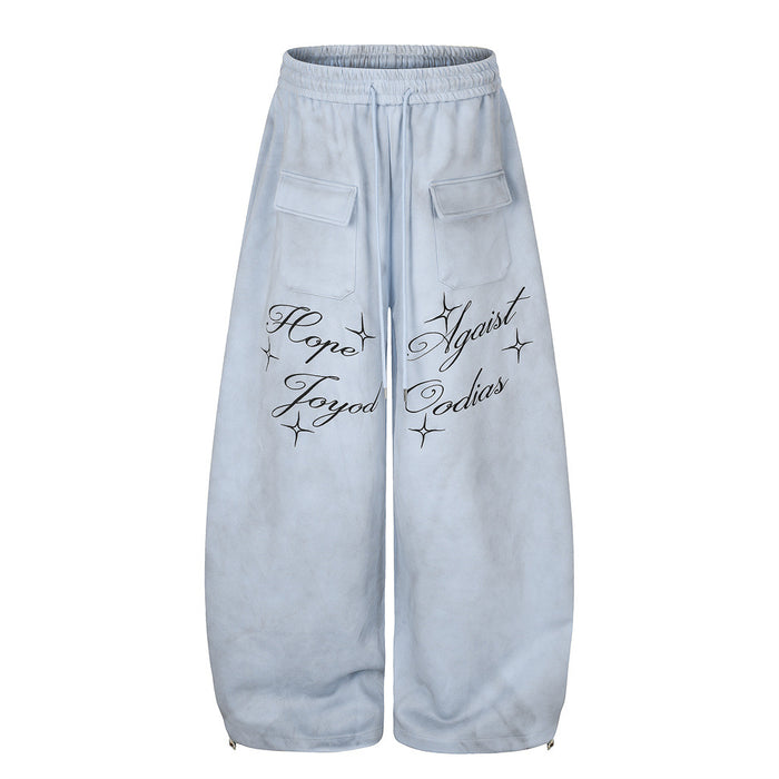 Front view of light blue wide-leg velour sweatpants with black script lettering and two cargo pockets