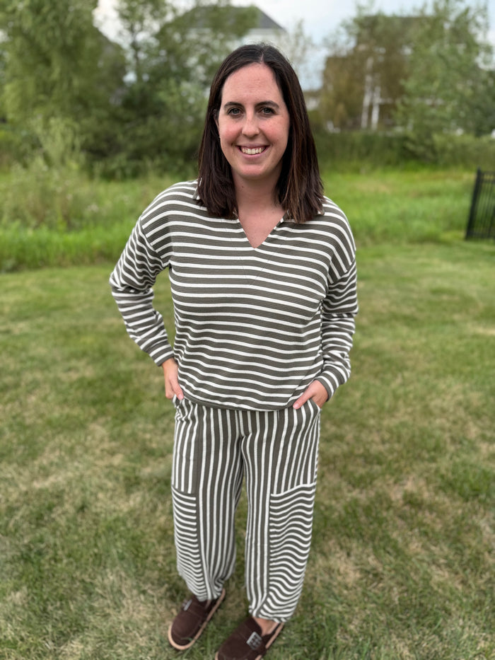 A woman wearing a matching two-piece loungewear set with olive green and white stripes, consisting of a long-sleeve V-neck top and striped pants.